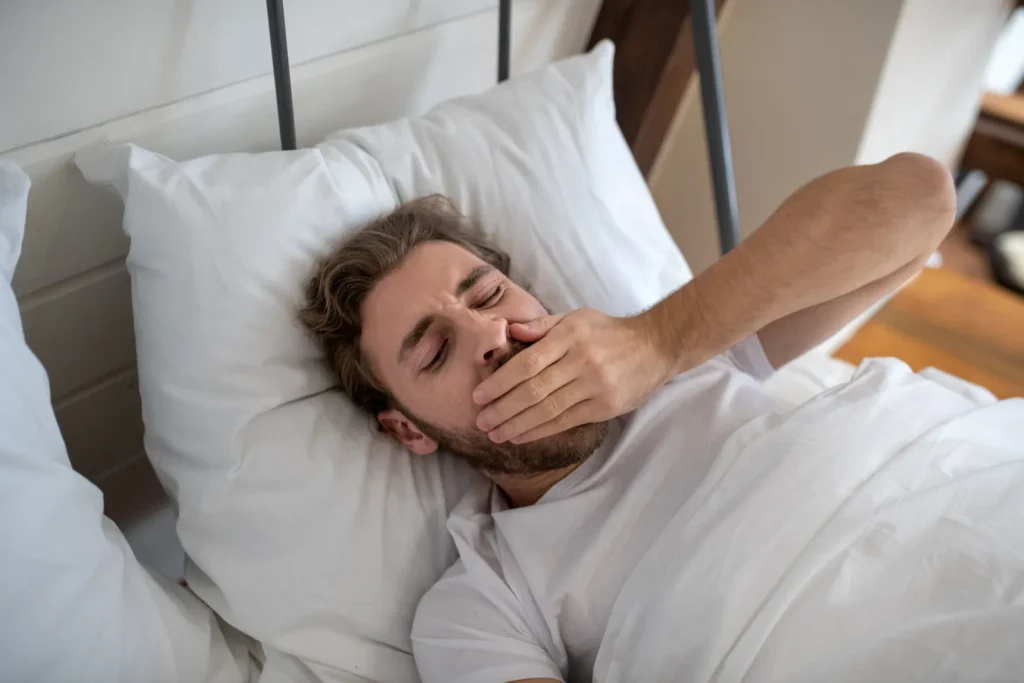 A man in bed covering a yawn